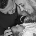 black and white image, close up family, mum dad baby, looking at each other, dad stroking baby head, mum long hair