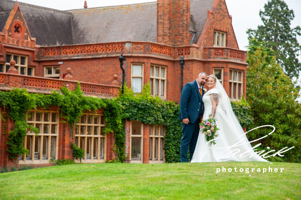tudor mansion, cambridge, exterior shot, grounds, front holmewood hall, bride, groom, bouquet, grass, building, mansion https://www.holmewood-hall.co.uk/venue/