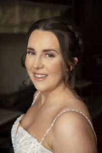 smiling bride, side view, made up, dark hair, brown eyes, strappy bride dress, dark background