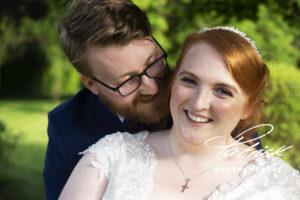 bride foreground, groom background, smiling, close up, bride eye contact camera, groom looking at bride