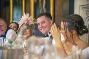 groom smiling, blushing, amongst bride and mother in law, at table, wedding breakfast, bride laughing