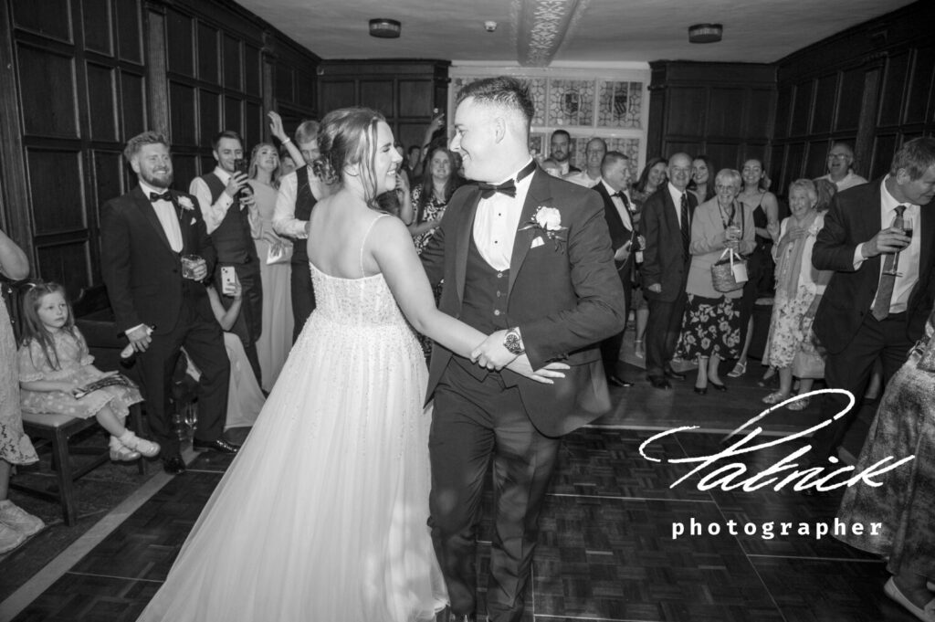 bride and groom first dance, holding hands, eye contact, full length, black and white, guests, onlookers background