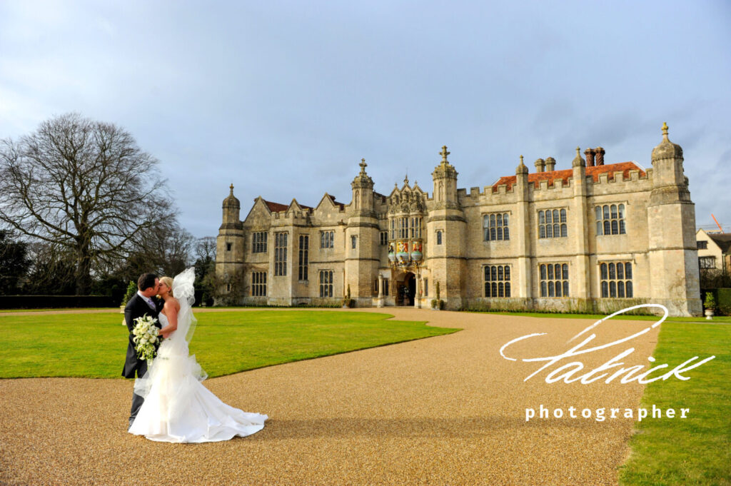bride and groom kiss in foreground. background is Hengrave Hall