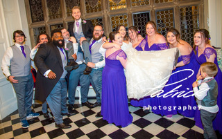 chequered black and white floor inside building, bridsmaids holding bride in air, page boy, grooms men holding groom in air. bridesmaids purple dresses, groomsmen in grey, night shot