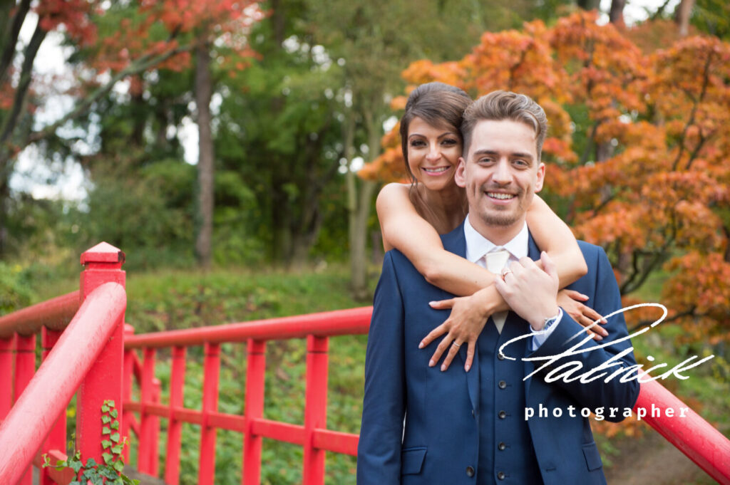 fanhams hall, red bridge, bride behind groom, arms over his shoulders. smiling. autumnal colours background, spring wedding!