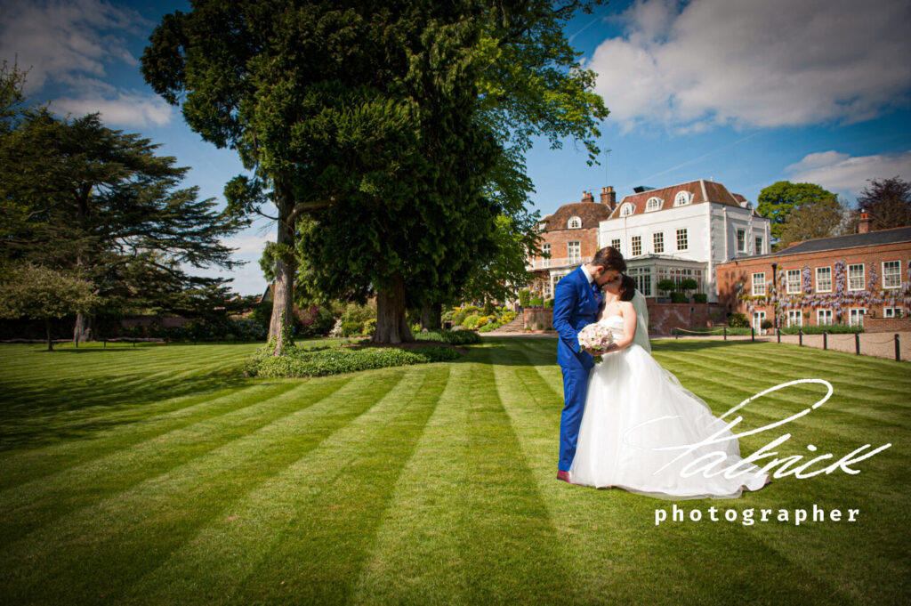 mansion house background, wedding venue, tree foreground, bride and groom embrace, kissing on manicured lawn at St michael's manor